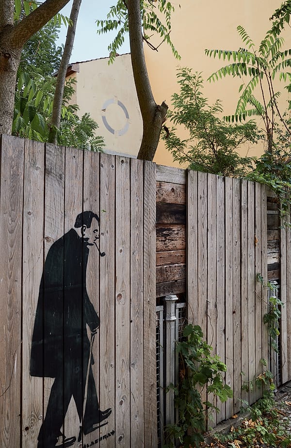 The Solitary Promenade - A stark, monochromatic figure traverses the weathered landscape of a wooden barrier, evoking a sense of quiet urban transit and transient existence