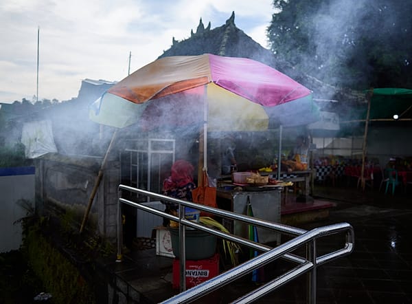 Market in the Mist - A veil of thick, white vapor softens the rigid geometry of a street-side structure, transforming a mundane culinary setup into an ethereal, dreamlike tableau